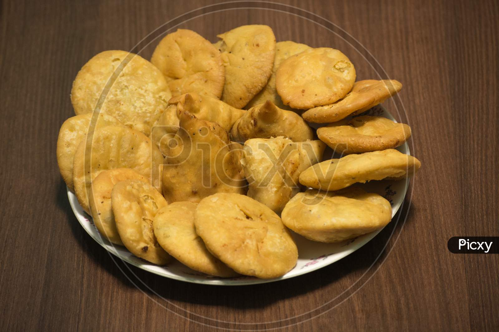 Samosa and matthi (mathari/kachori) Indian dish made of fine wheat flour stuffed with potato mesh served in glass dish with wooden background.