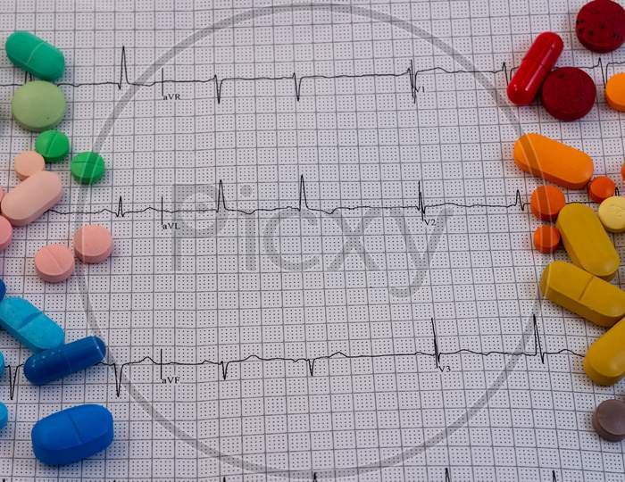 Pills And Medicines Of Different Colors And Sizes On An Electrocardiogram. Drugs For Human Consumption.