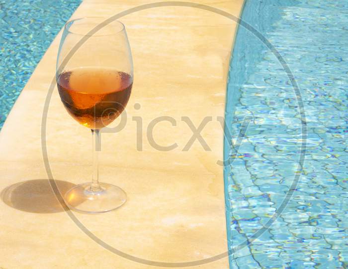 Glass Wine Glass On The Edge Of A Swimming Pool. Rose Wine In A Glass Goblet. Wealth Concept.