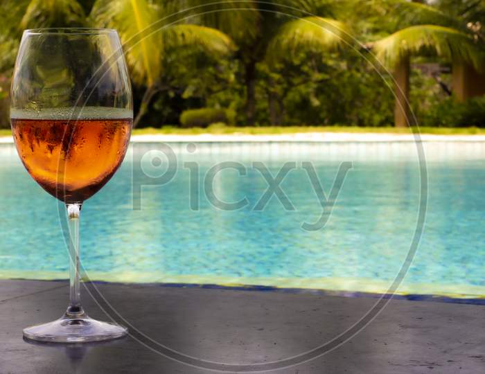 Crystal Glass With Fresh Rosé Wine Next To A Huge Pool Of Crystal Clear Water. Luxury Wealth And Vacation Concept.