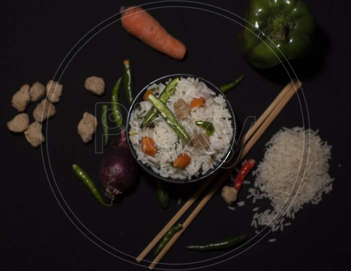 Top Down Image Of A Bowl Of A Steamed Rice And Vegetables Decorated With Veggies, Grains, Chopsticks And Spoon In A Black Copy Space Background. Food Photography.
