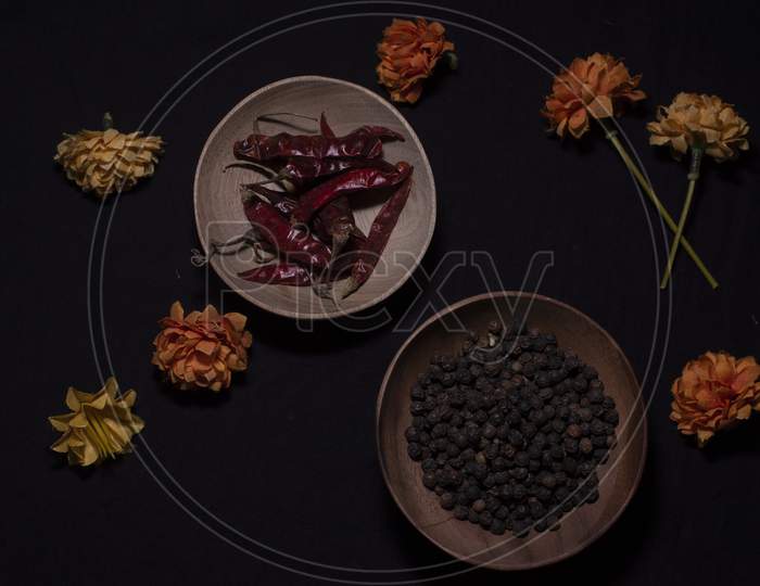 Top Down Image Of Black Pepper And Dried Chili In A Wooden Bowl Decorated With Dry Flowers In A Dark Copy Space Background.