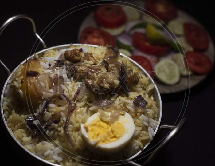 Indian Spicy Dish Biryani With Egg, Potato And Chicken In A Pot Along With Fresh Salads In Dark Copy Space Background. Food And Object Photography.
