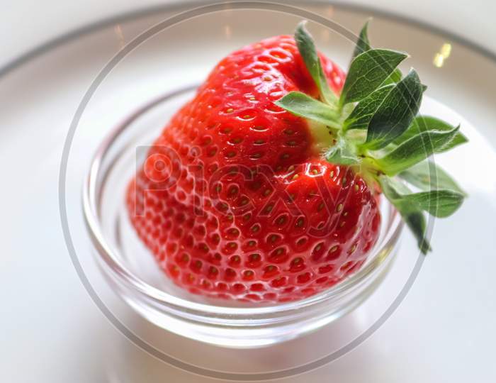 Strawberries with leaves on a plate in a glas bowl. Isolated on a white background.
