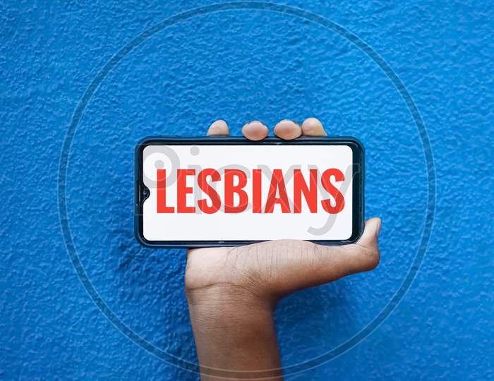 Lesbians Word On Smart Phone Screen Isolated On Blue Background With Copy Space For Text. Person Holding Mobile On His Hand And Showing Front Of Lesbians.(Lesbi, Gay, Bisexual, Transgender).