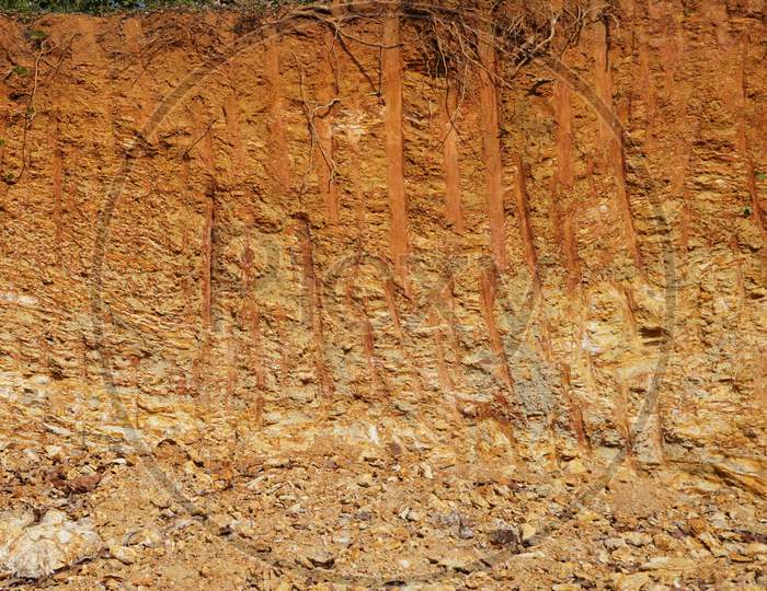 Deforestation close up with roots, rocks showing in sunlight. Red and yellow rocks where soil was dug from forest using an excavator in construction site. Sand excavation concept.