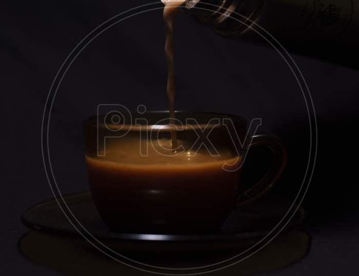 Hot Infused Tea/Coffee Being Poured In A Transparent Glass Cup And Soccer Kept In Black Copy Space Background. Indian Beverages And Food Photography.