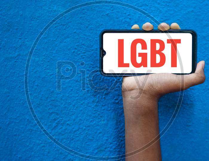 Lgbt Word On Smart Phone Screen Isolated On Blue Background With Copy Space For Text. Person Holding Mobile On His Hand And Showing Front Of Lgbt (Lesbi, Gay, Bisexual, Transgender).