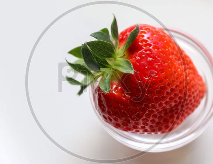 Strawberries with leaves on a plate in a glas bowl. Isolated on a white background.