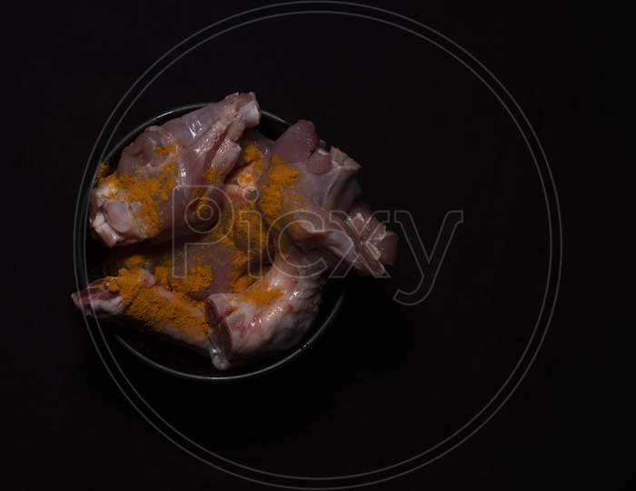 Top Down Image Of A Bowl Of Raw Chicken Pieces Sprinkled With Turmeric Powder In A Dark Copy Space Background. Food And Product Photography.
