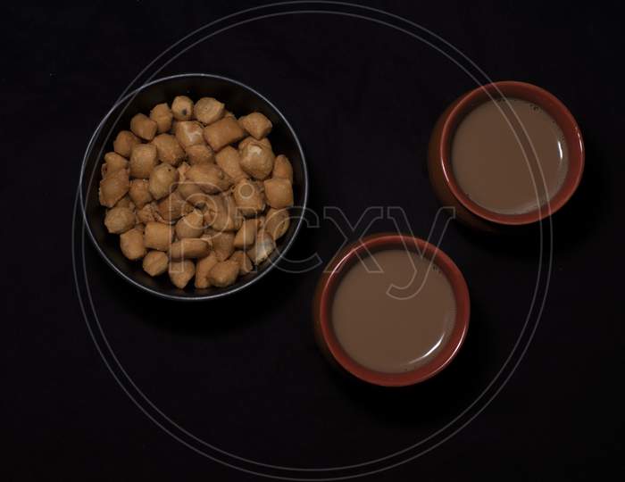 Top Down Image Of Infused Tea In Earthen Cups Along With A Bowl Of Snacks Kept In Black Copy Space Background. Indian Beverages And Food Photography.