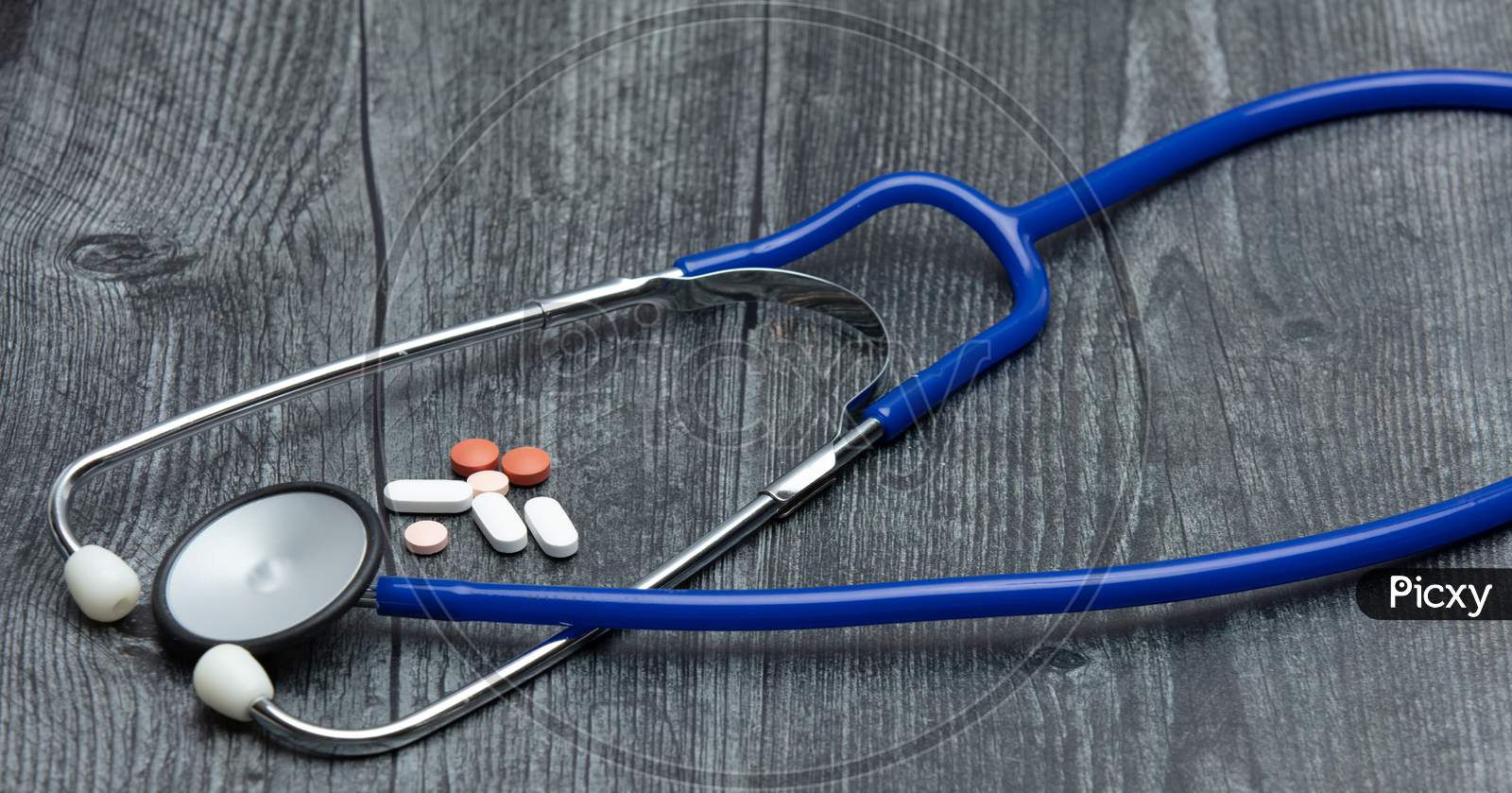A Blue Medical Stethoscope And A Variety Of Medical Pills Sit On A Wooden Table.
