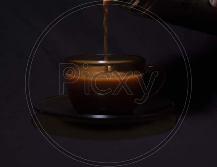 Hot Infused Tea/Coffee Being Poured In A Transparent Glass Cup And Soccer Kept In Black Copy Space Background. Indian Beverages And Food Photography.
