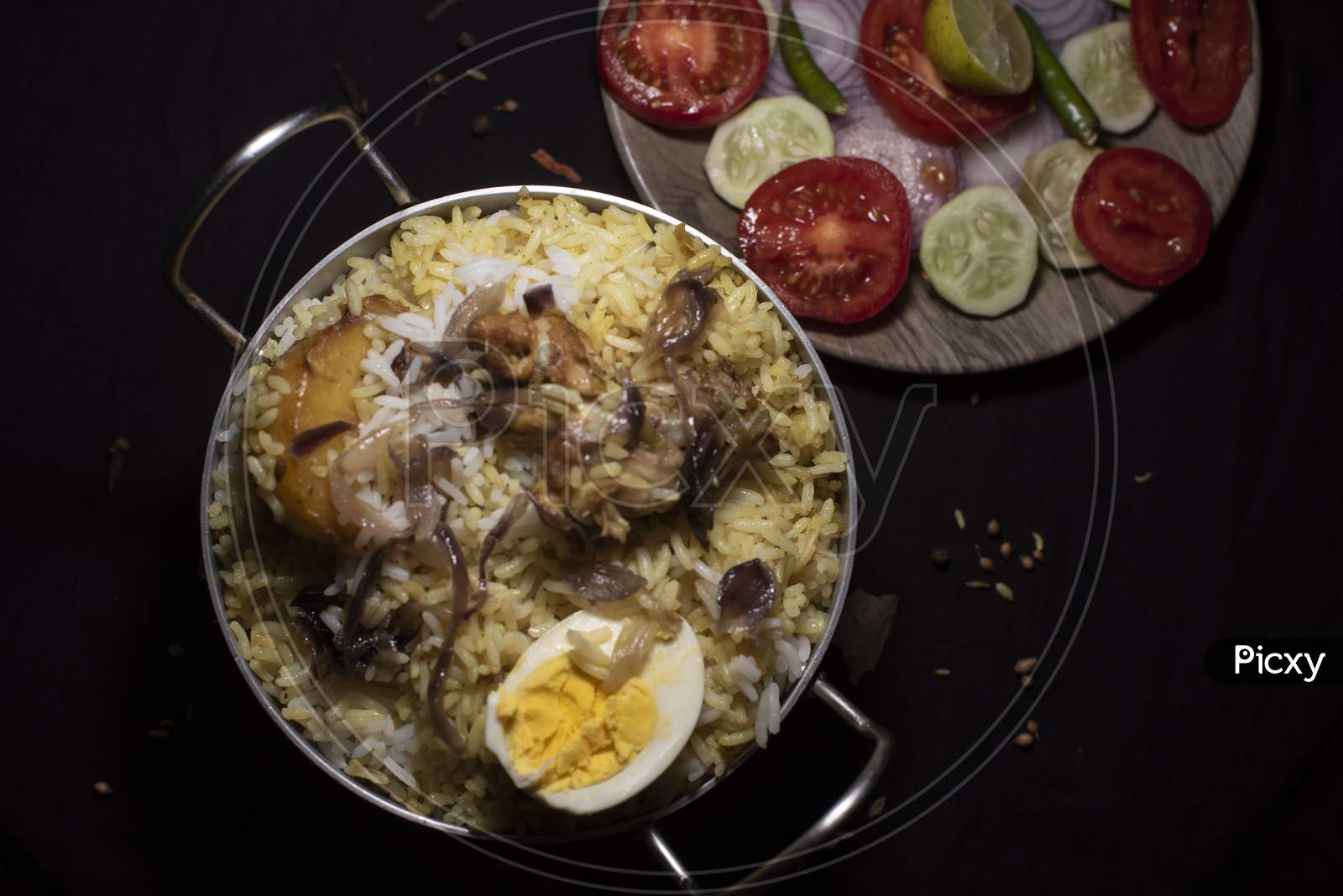Indian Spicy Dish Biryani With Egg, Potato And Chicken In A Pot Along With Fresh Salads In Dark Copy Space Background. Food And Object Photography.