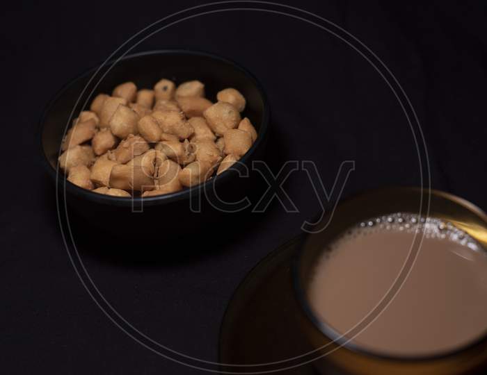 Hot Infused Tea In A Transparent Glass Cup And Soccer Along With A Bowl Of Snacks Kept In Black Copy Space Background. Indian Beverages And Food Photography.