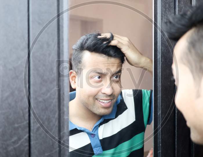 An Indian In Casual T-Shirt Male Looking At His Reflection In Mirror And Hair Styling
