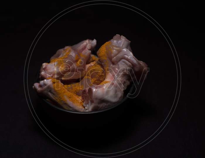 A Bowl Of Raw Chicken Pieces Sprinkled With Turmeric Powder In A Dark Copy Space Background. Food And Product Photography.