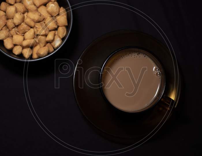 Top Down Image Of Infused Tea In A Transparent Glass Cup And Soccer Along With A Bowl Of Snacks Kept In Black Copy Space Background. Indian Beverages And Food Photography.