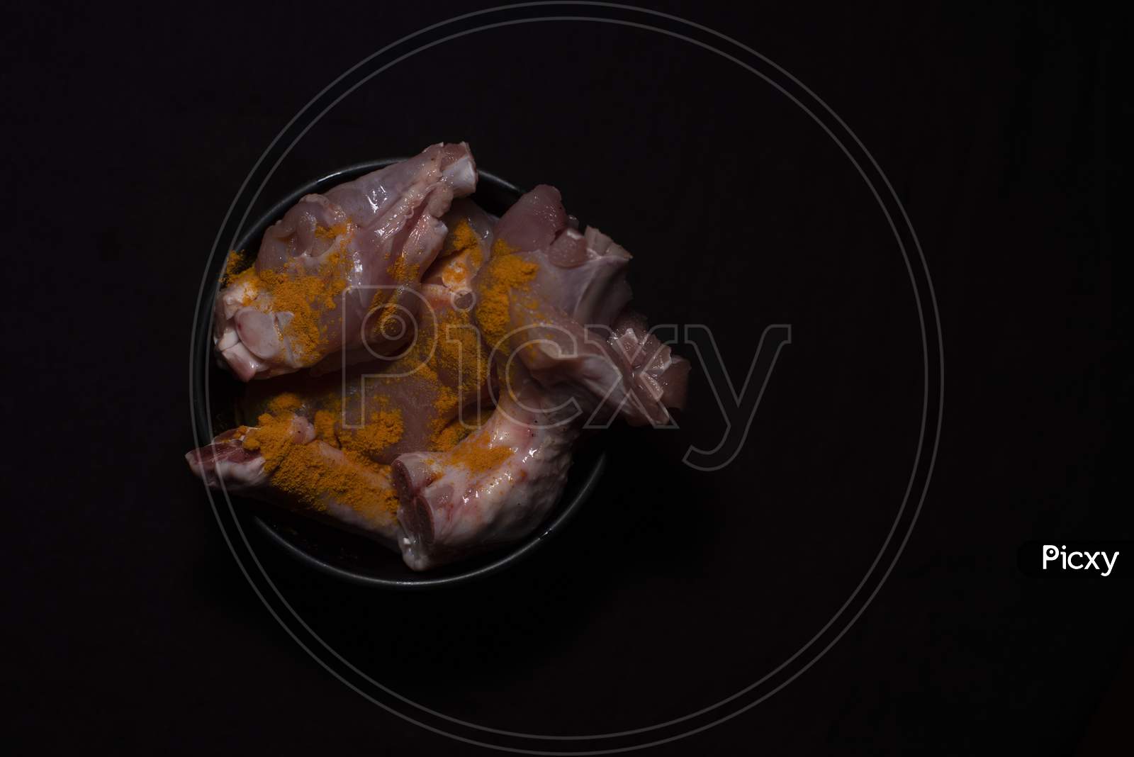 Top Down Image Of A Bowl Of Raw Chicken Pieces Sprinkled With Turmeric Powder In A Dark Copy Space Background. Food And Product Photography.
