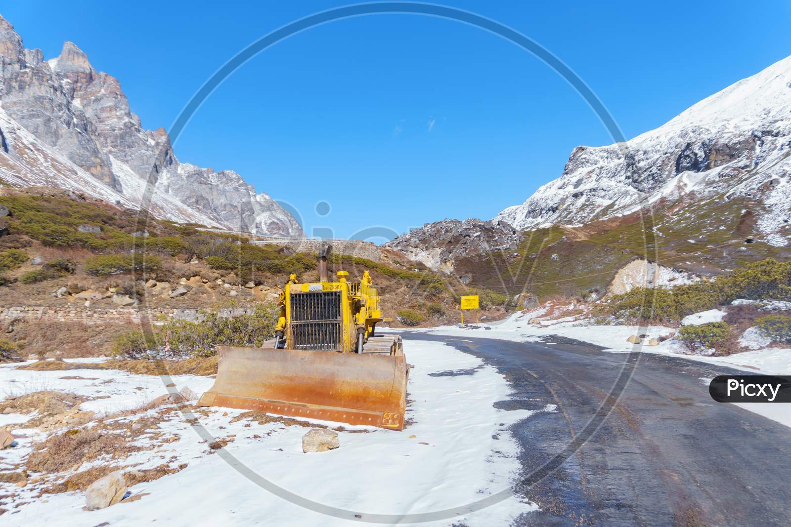 a yellow bulldozer waiting for landslides and heavy snow on the mountain road