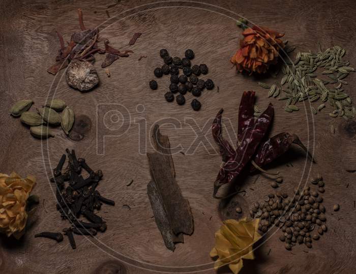 Top Down Image Of Different Whole Spices Decorated With Dried Flowers In A Wooden Background.