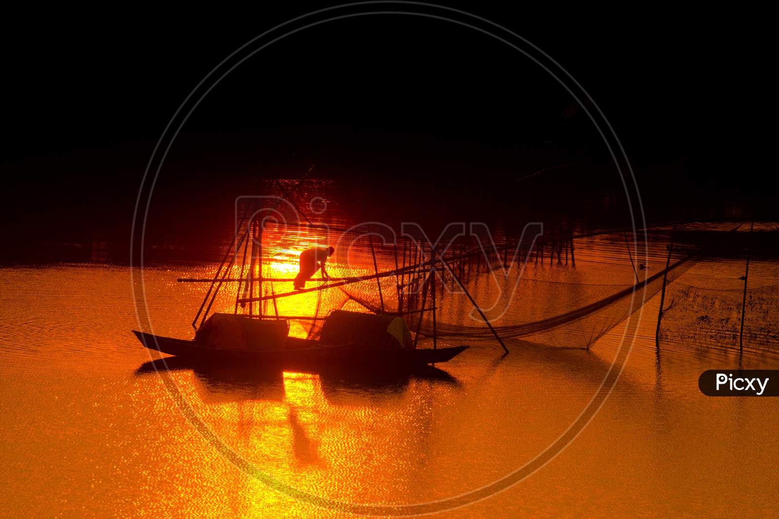 A Traditional Fisherman Catching The Fish Into The Golden Twilight At Sunset Time.
