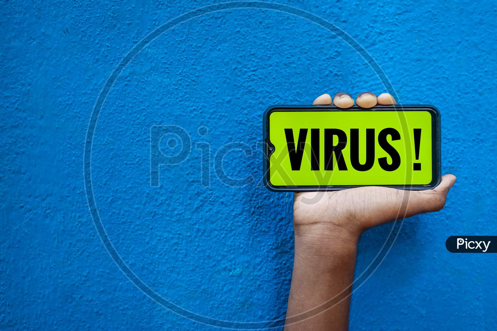 Virus / Covid-19 Wording On Smart Phone Screen Isolated On Blue Background With Copy Space For Text. Person Holding Mobile On His Hand And Showing Front Of The Screen For Corona Virus Wording.