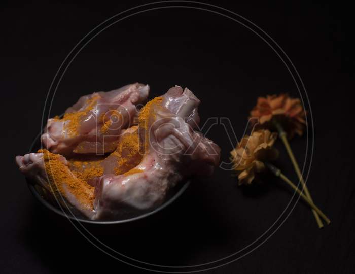 A Bowl Of Raw Chicken Pieces Sprinkled With Turmeric Powder Decorated With Dried Flowers In A Dark Copy Space Background. Food And Product Photography.
