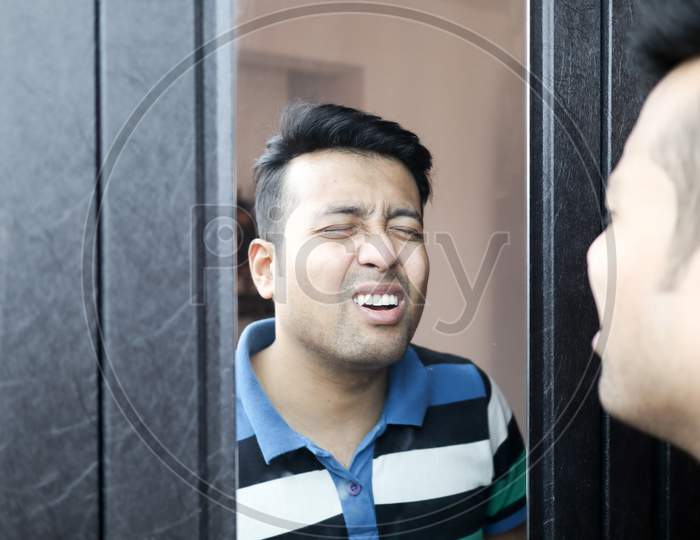 An Indian Male In Casual T-Shirt Giving Wierd Expression At His Reflection In Mirror
