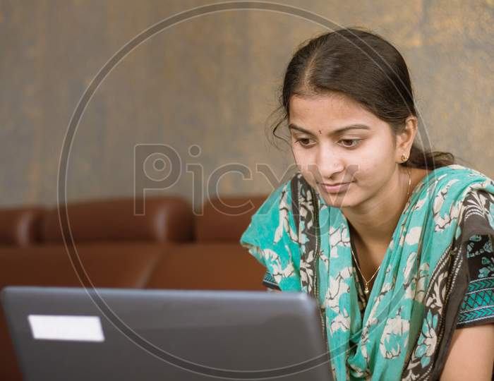 Smiling Indian Girl Student Or Employee Busy On Laptop Sit At Home In Casual Dress, Happy Woman Studying, E-Learning, Using Online Software Or Technology App For Work, Education Concept