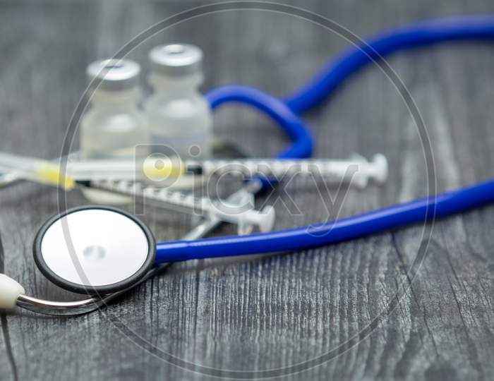 A Blue Medical Stethoscope, Syringes And Vials Sit On A Wooden Surface.