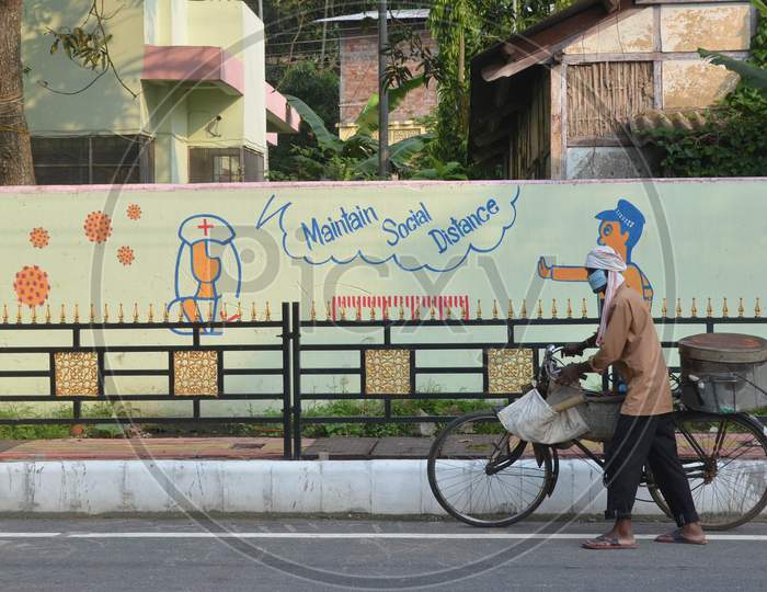 A Fish Seller Wearing A Face Mask Pushes His Bicycle As he Walks Past A Mural During Nationwide Lockdown Amidst Coronavirus or COVID-19 Pandemic  In Guwahati District Of Assam,India