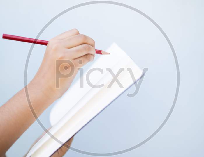 Child Hand Writing On A Blank Notebook Against Plain Background