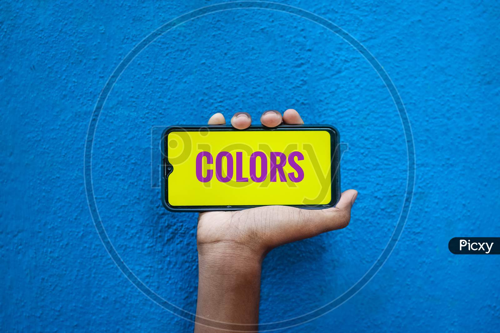 Colors Word On Smart Phone Screen Isolated On Blue Background With Copy Space For Text. Person Holding Mobile On His Hand And Showing Front Of The Screen Wording Colors.