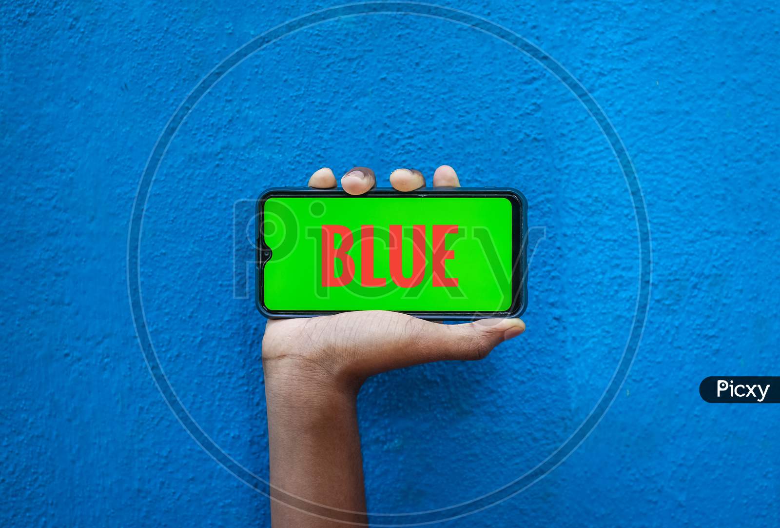 Blue Word On Orange Color In Smart Phone Screen Isolated On Blue Background With Copy Space For Text. Person Holding Mobile On His Hand And Showing Front Of The Screen Word Blue.