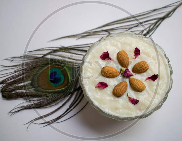 Top View Of Indian Dessert Kheer/Khir (Rice Pudding) Made From Condensed Milk, Rice, Sugar And Dry Fruits. Garnished With Rose Petals Almonds In Shape Of Flower Design And Peacock Feather Food Decoration