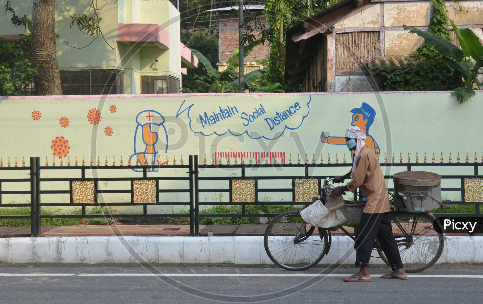 A Fish Seller Wearing A Face Mask Pushes His Bicycle As he Walks Past A Mural During Nationwide Lockdown Amidst Coronavirus or COVID-19 Pandemic  In Guwahati District Of Assam,India