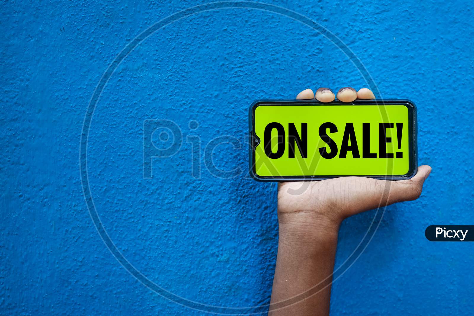 On Sale Wording On Smart Phone Screen Isolated On Blue Background With Copy Space For Text. Person Holding Mobile On His Hand And Showing Front Of The Screen Word On Sale