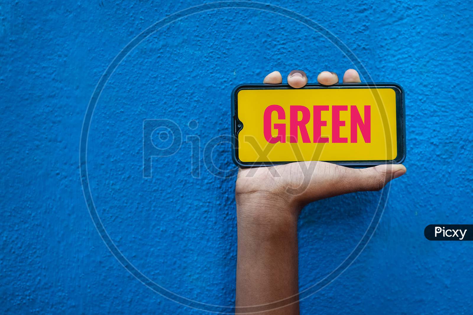 Green Word On Red Color In Smart Phone Screen Isolated On Blue Background With Copy Space For Text. Person Holding Mobile On His Hand And Showing Front Of The Screen Word Green.