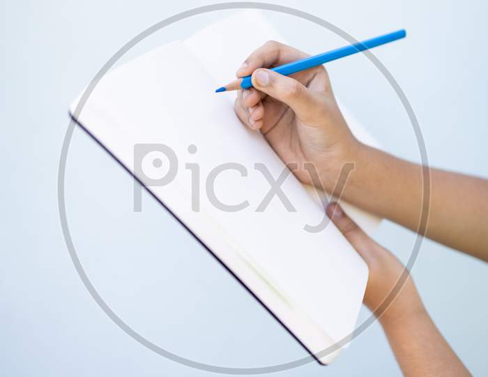 Child Hand Writing On A Blank Notebook Against Plain Background