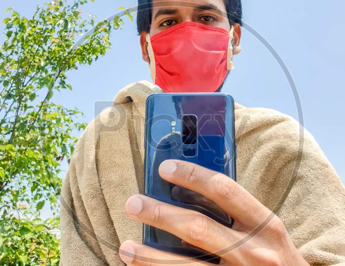 To protect against coronavirus, a indian young man wearing a face mask capture a photo of himself with a phone in front of a mirror with sensor / Lens dust