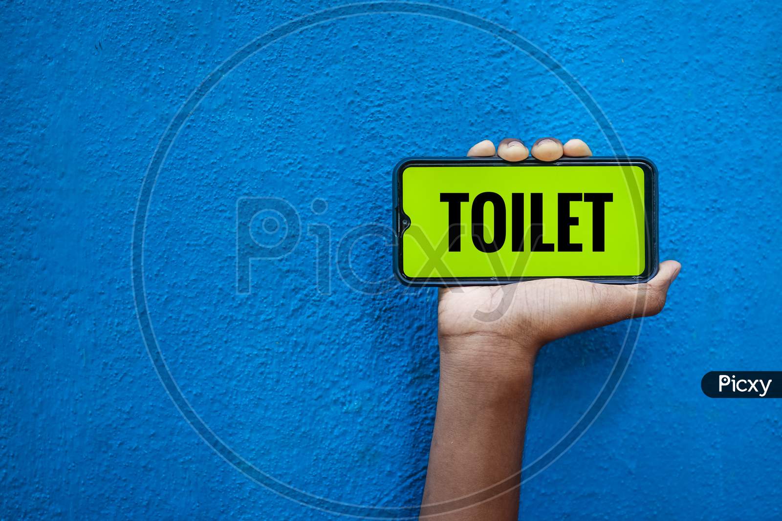 Toilet Wording On Smart Phone Screen Isolated On Blue Background With Copy Space For Text. Person Holding Mobile On His Hand And Showing Front Of The Screen Word Toilet.