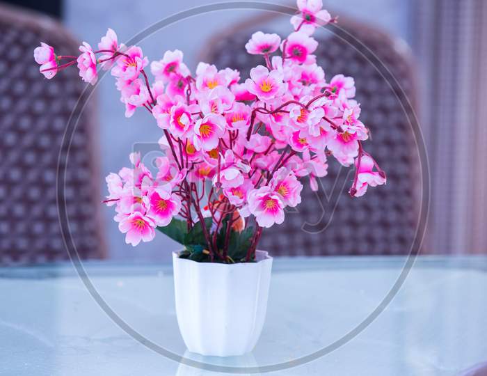 Pink Artificial Flower In A White Vase On A White Glass Table