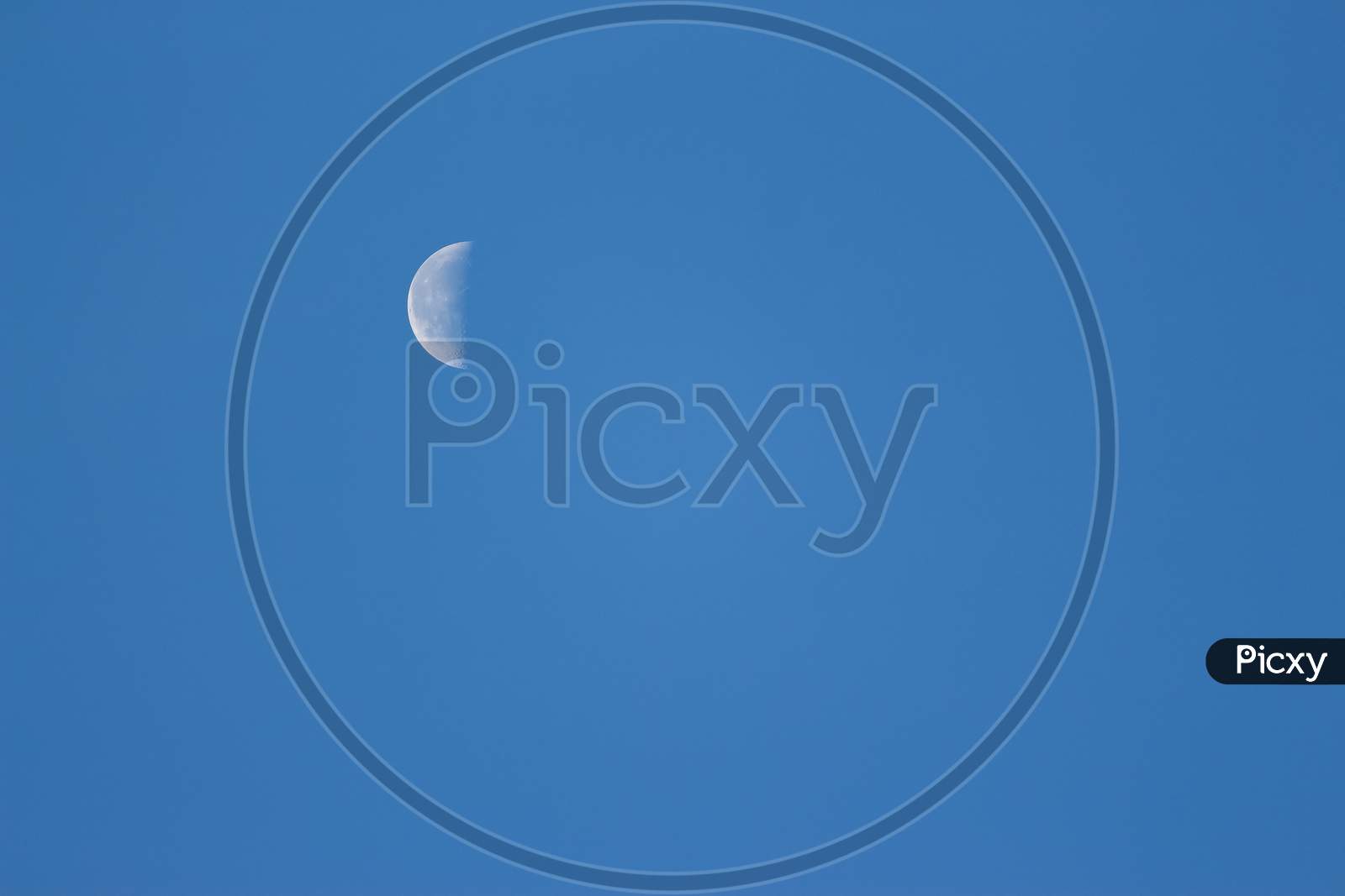 Moon Lunar / Luna On The Blue Sky. Half Lunar Moon In A Clear Daylight Sky. Earth Moon Lunar On Day Time With Copy Space For Text. Luna On The Day Sky. Selene .Cynthia