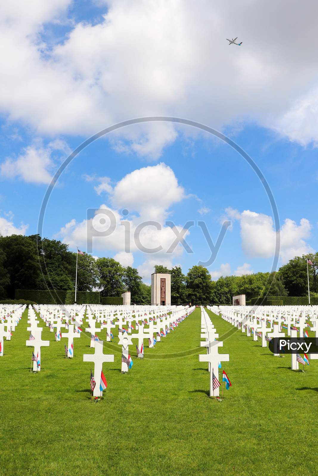Rows Of Headstones At A Military Cemetery With An Airplane Flying Through The Clouds
