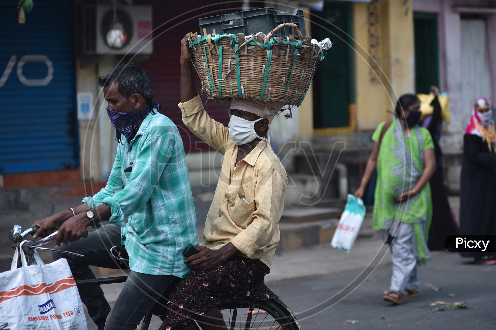 A Man Carries A Basket Over His Head As He Rides Pillion On A Bicycle While Returning Home From A Market During The Nationwide Lockdown Amid Coronavirus Pandemic In Vijayawada.