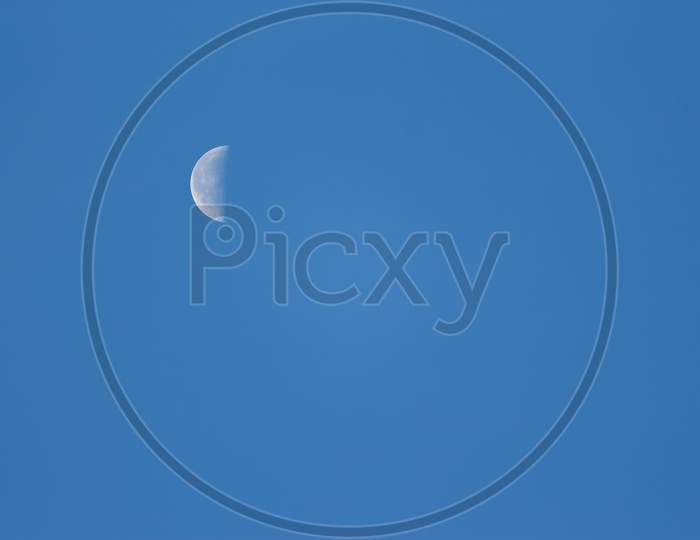 Moon Lunar / Luna On The Blue Sky. Half Lunar Moon In A Clear Daylight Sky. Earth Moon Lunar On Day Time With Copy Space For Text. Luna On The Day Sky. Selene .Cynthia