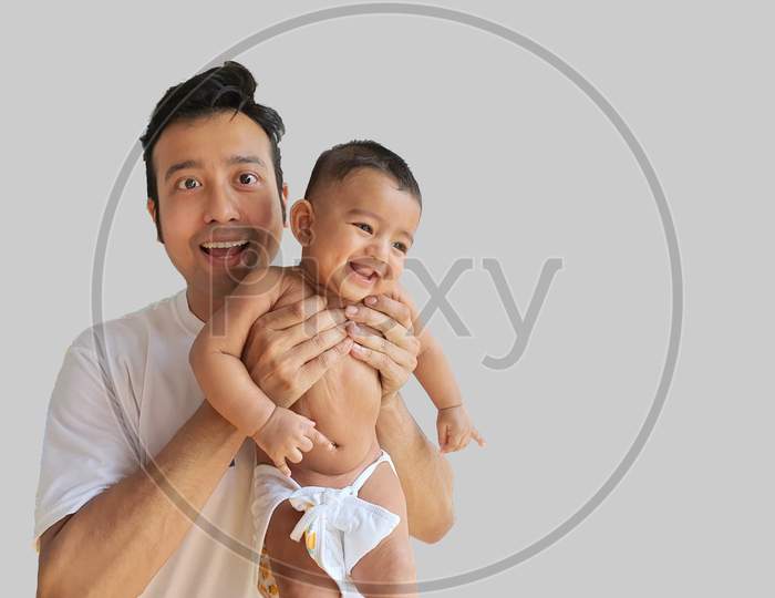 A Smiling Little Baby Boy Held By His Father With Grey Background And Space For Text.