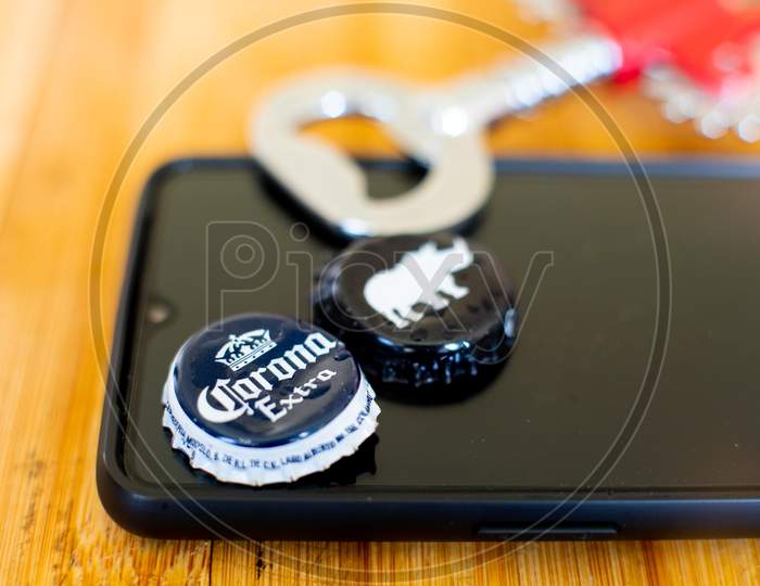 Mobile Phone On A Wooden Board With Beer Bottle Caps And An Opener Showing Online App For Alcohol Home Delivery.