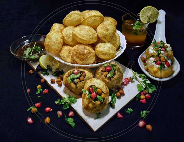 Mouthwatering panipuri garnished with coriander leaves, boiled chickpeas,pomegranate seeds and curd on a black background.